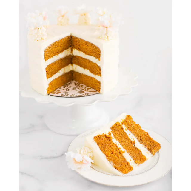 Layered carrot cake with frosting on a stand and a slice served on a plate