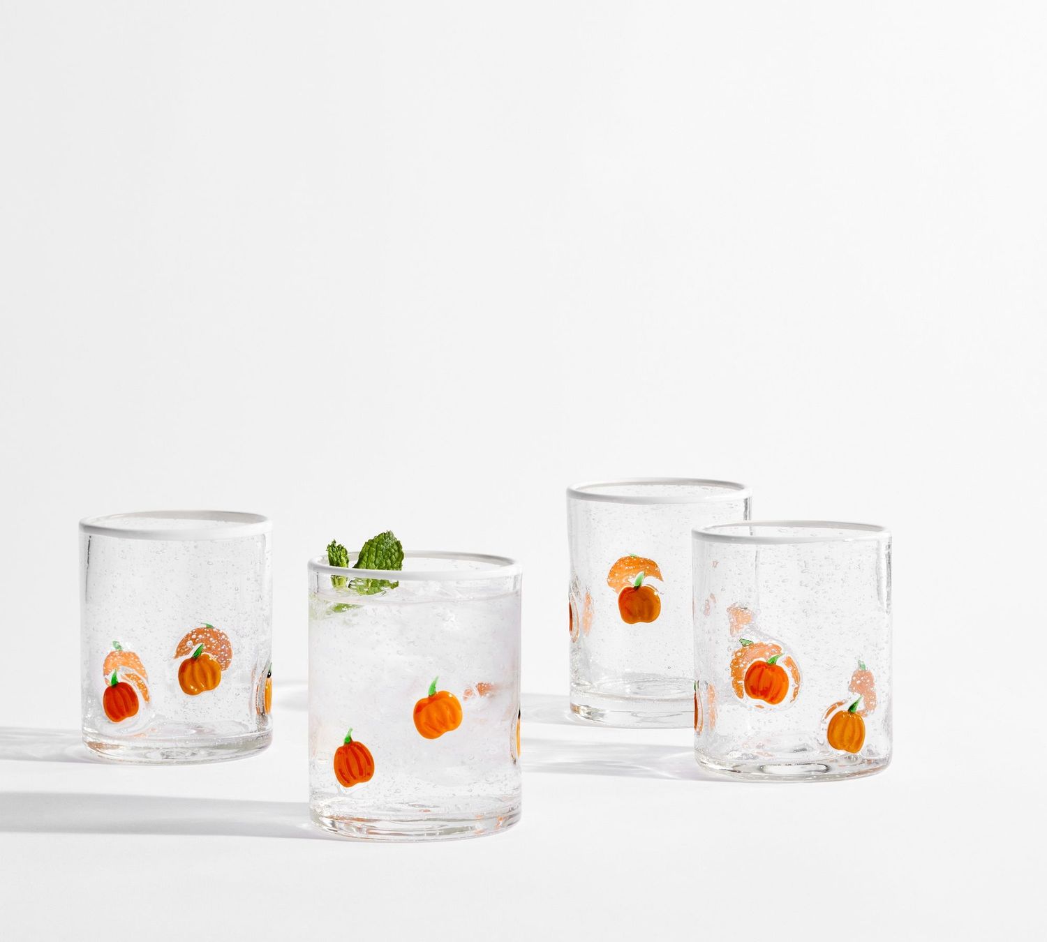 Four drinking glasses decorated with pumpkin designs one containing a drink and mint garnish