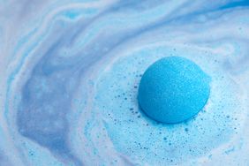A blue bath bomb in water creating a swirling effect with foam