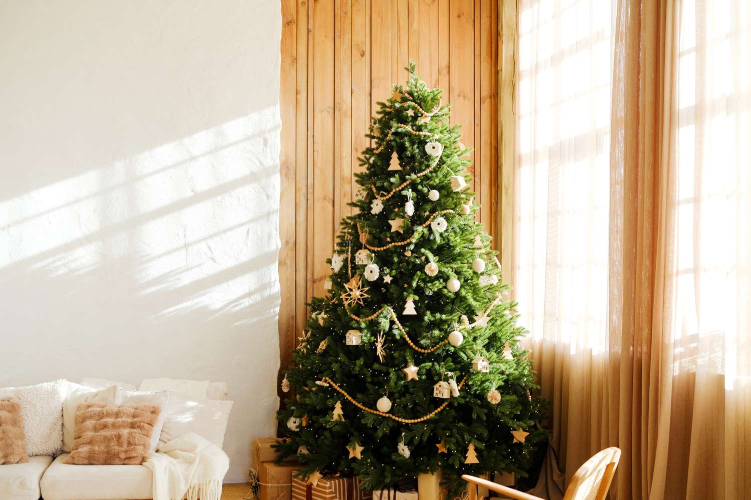 Decorated evergreen tree with ornaments and string lights indoors with sunlight streaming through