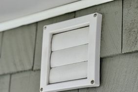 A closeup view of a white exterior vent installed on the wall of a building