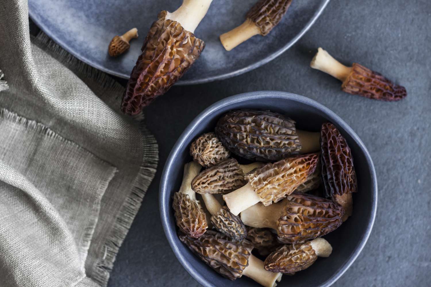 Bowls containing morel mushrooms on a surface with a cloth nearby