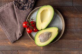 A sliced avocado and red tomatoes on a plate wooden surface and cloth nearby