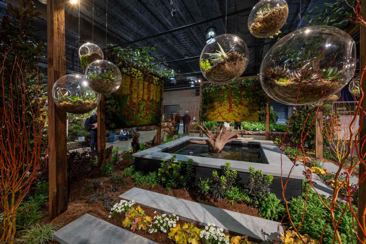 Indoor garden display featuring suspended glass globes with plants a water feature and lush greenery