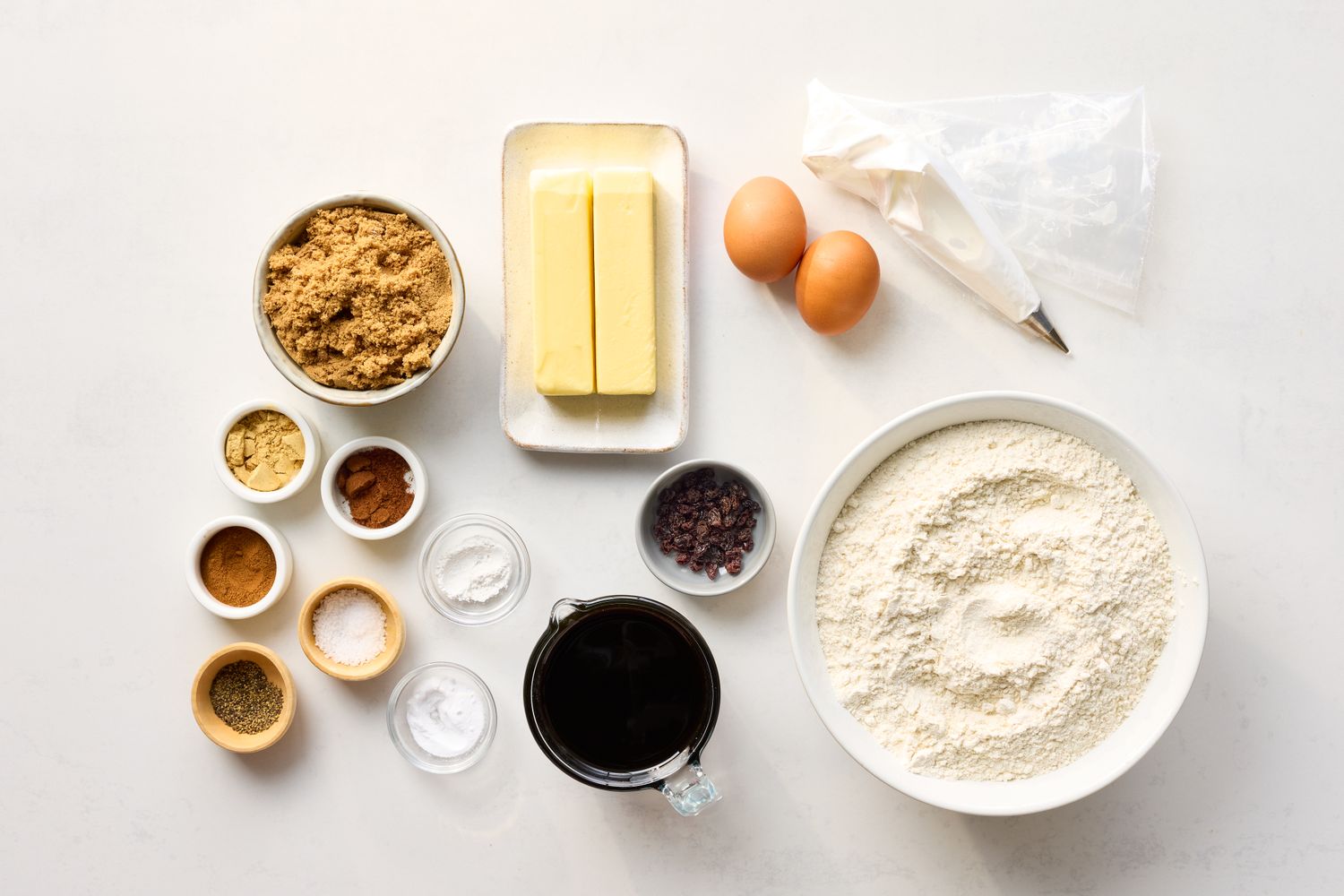 Ingredients for making gingerbread cookies arranged on a surface including eggs butter flour and spices