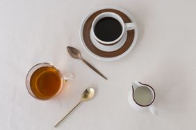 Cup of coffee glass of tea small pitcher of milk and two spoons on a table