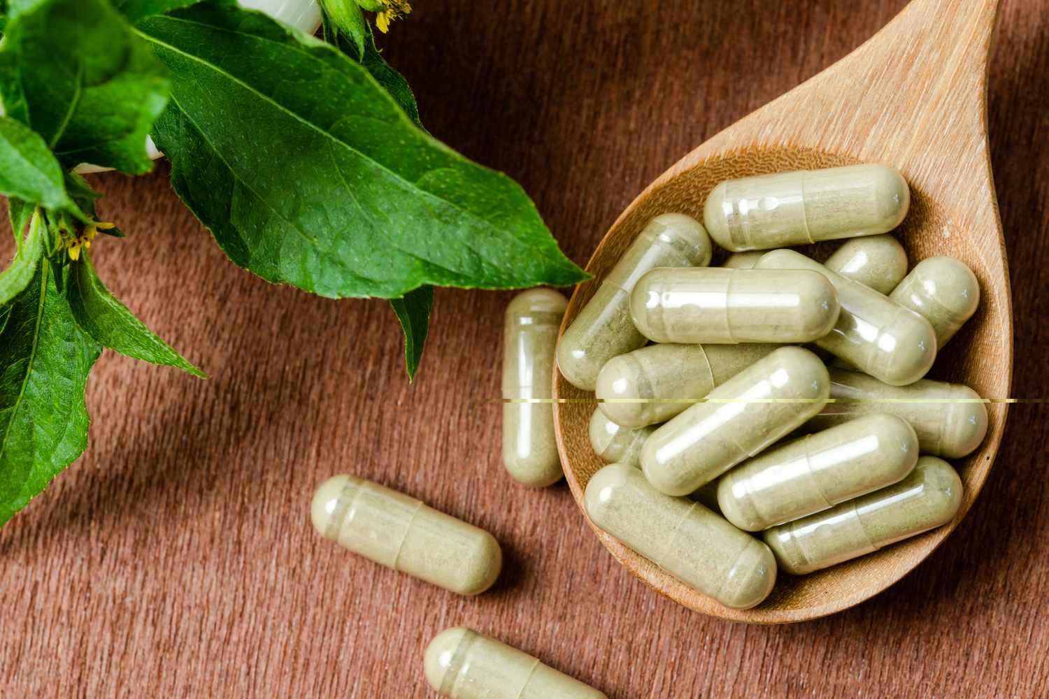 Wooden spoon holding green powder capsules with leaves nearby