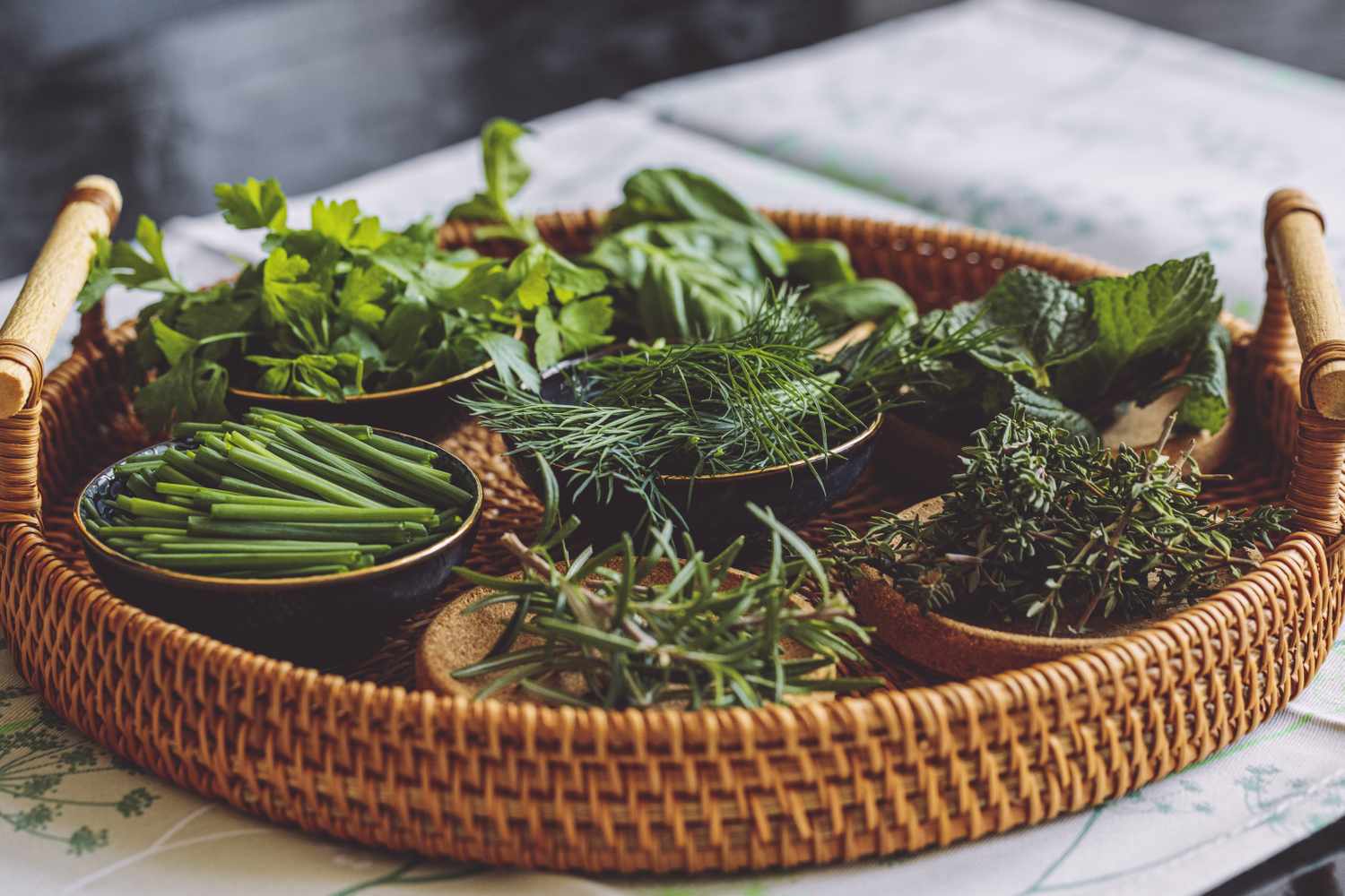 A wicker tray with fresh green herbs in small bowls on a table