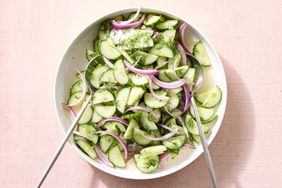 A bowl of cucumber red onion and dill salad with tossing utensils