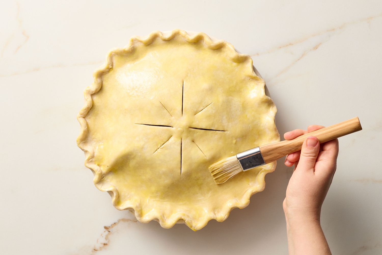 Hand brushing pie crust before baking, the pie has decorative slits on top