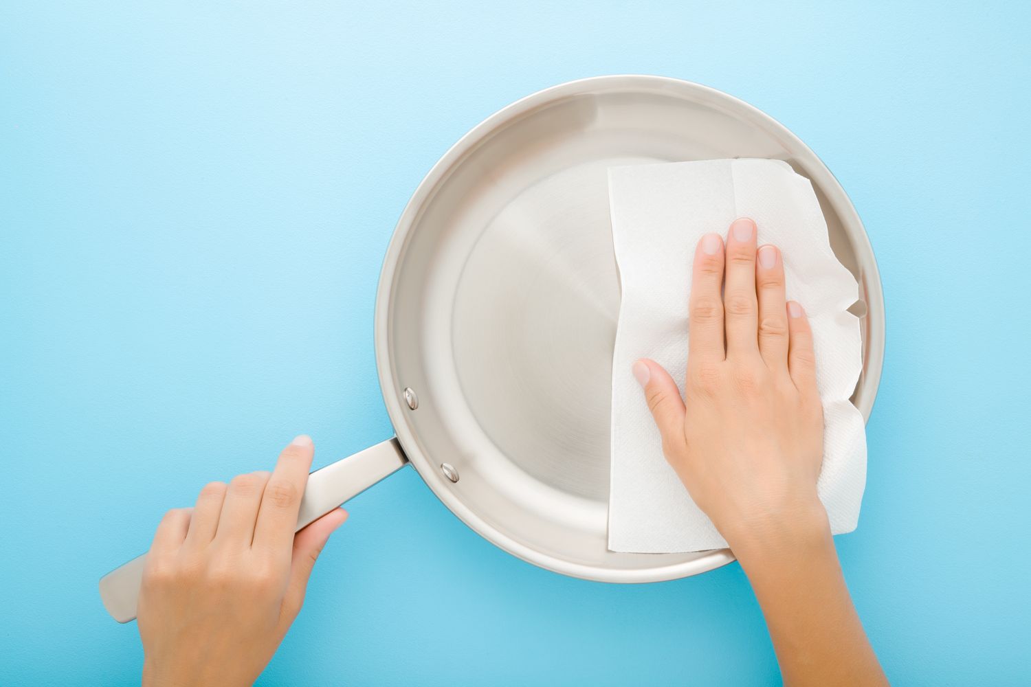 A hand cleaning a frying pan with a paper towel