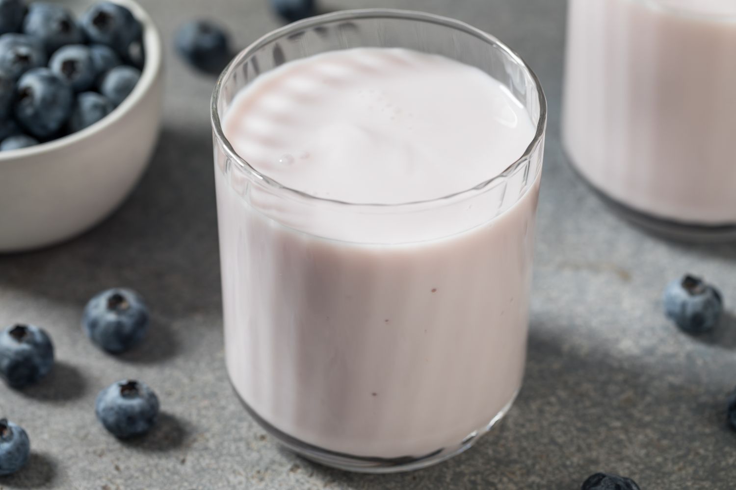 A glass of yogurt with blueberries in a bowl and scattered on a table