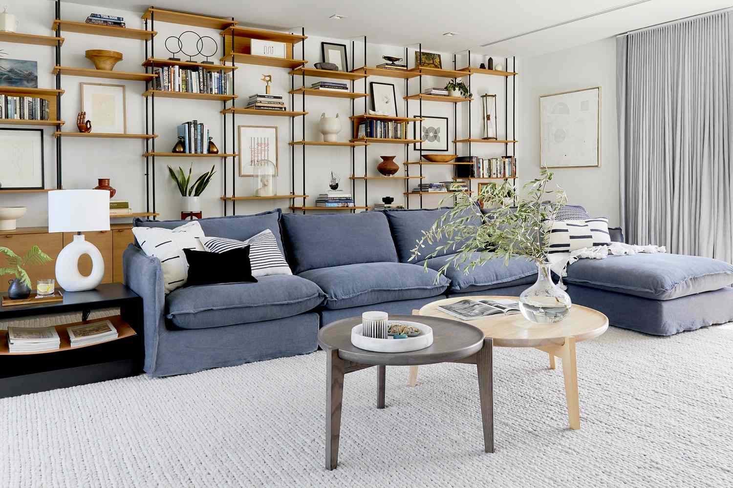 A modern living room with a blue sectional sofa minimalist shelves and a neutral carpeted floor