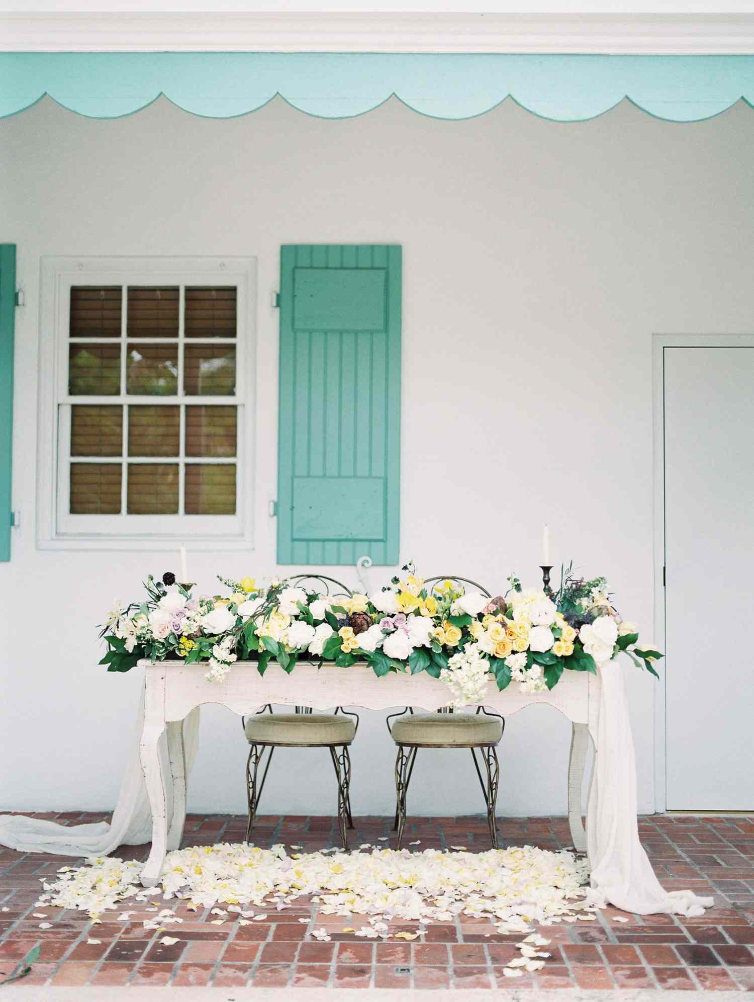 sweetheart table outdoor blue awning floral arrangements and flower petals