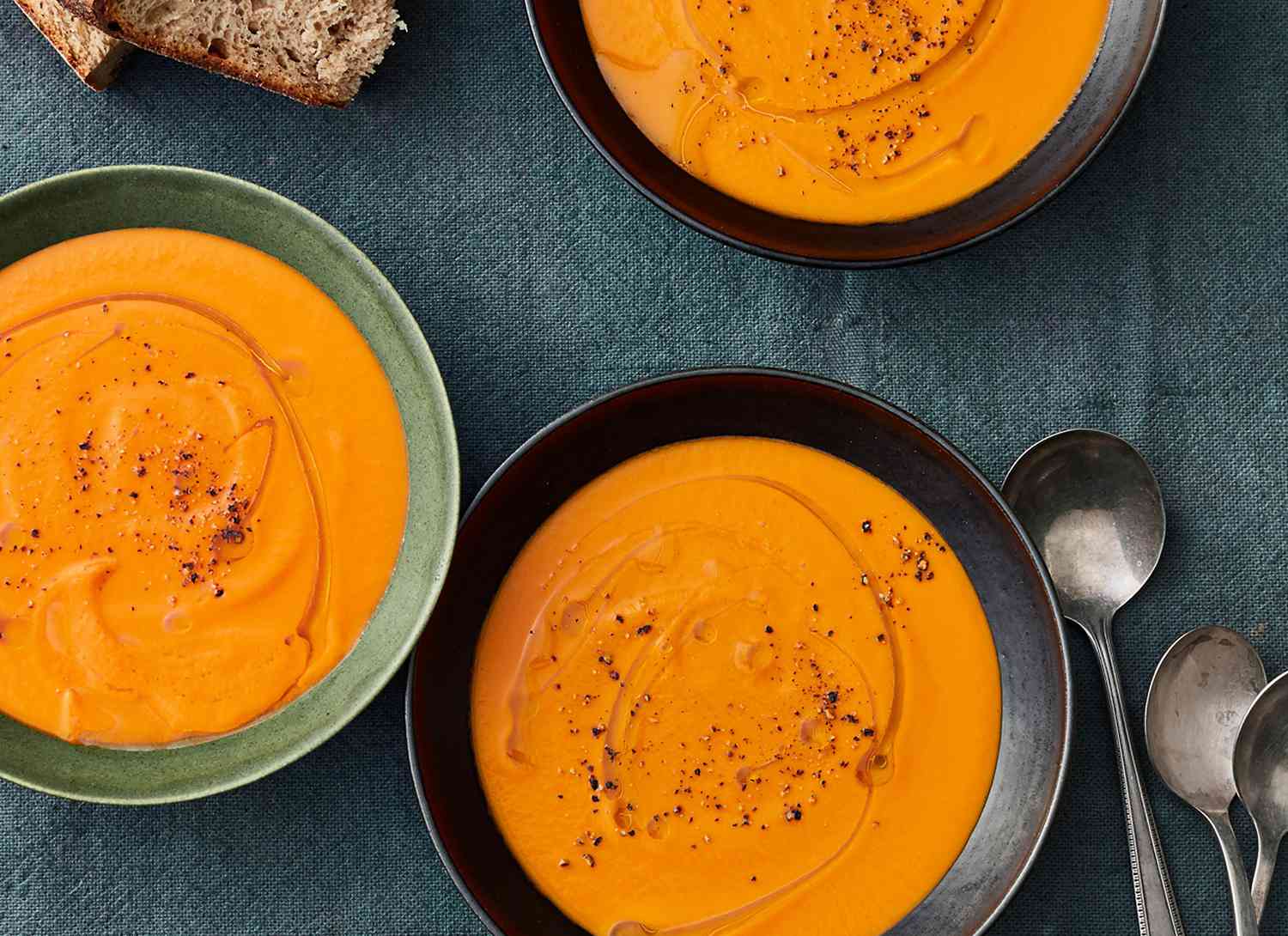 overhead view of bowls of carrot and tomato soup on blue linen
