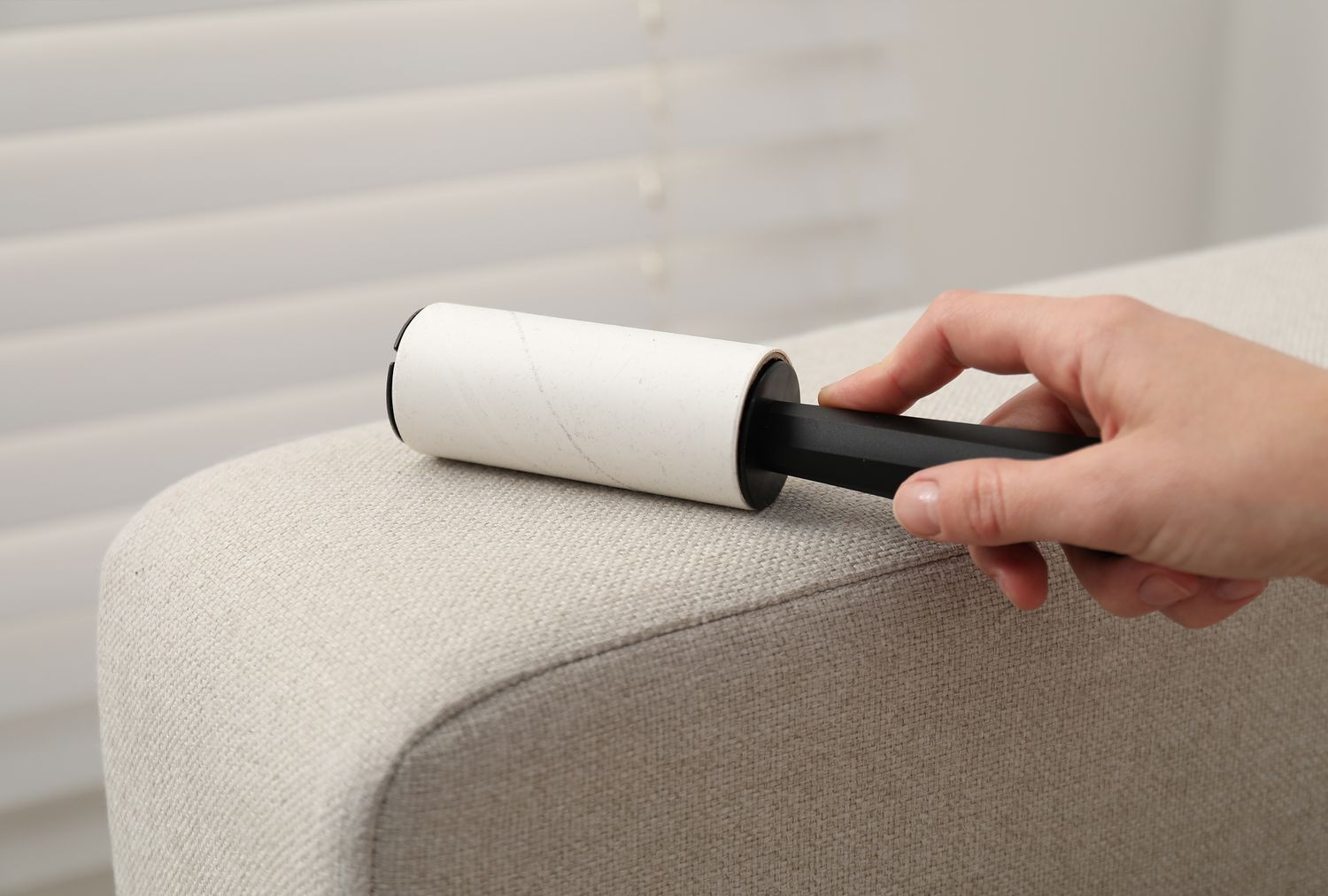 A hand using a lint roller on a couch armrest