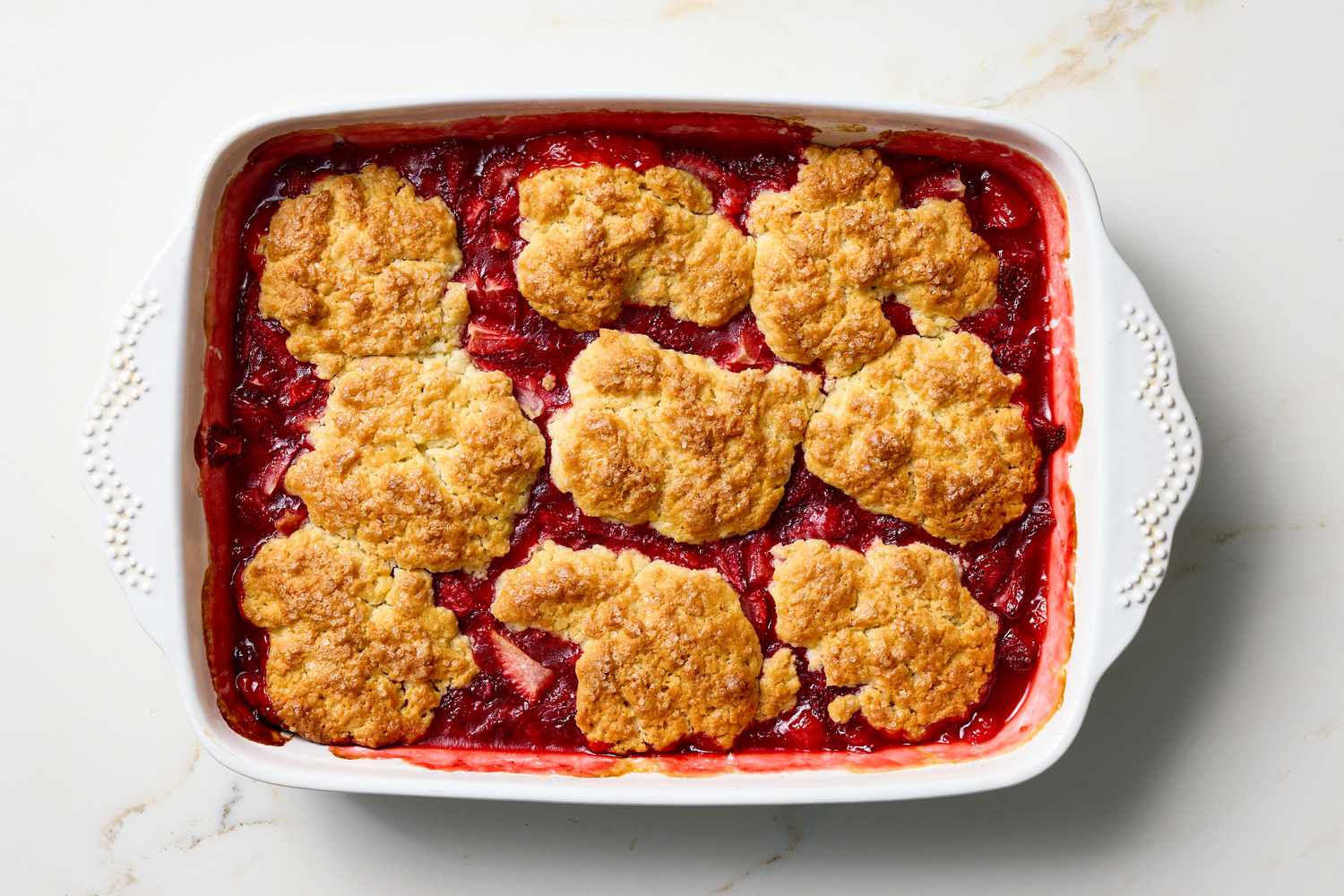 Strawberry cobbler in a white baking dish on a marble surface