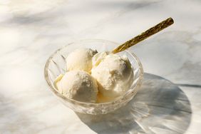 A glass bowl with three scoops of vanilla ice cream and a golden spoon