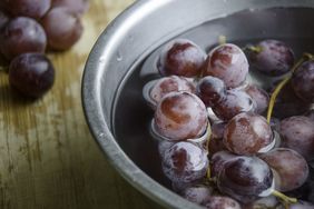 Bunch of grapes get washed in a bowl of cold water on wooden table