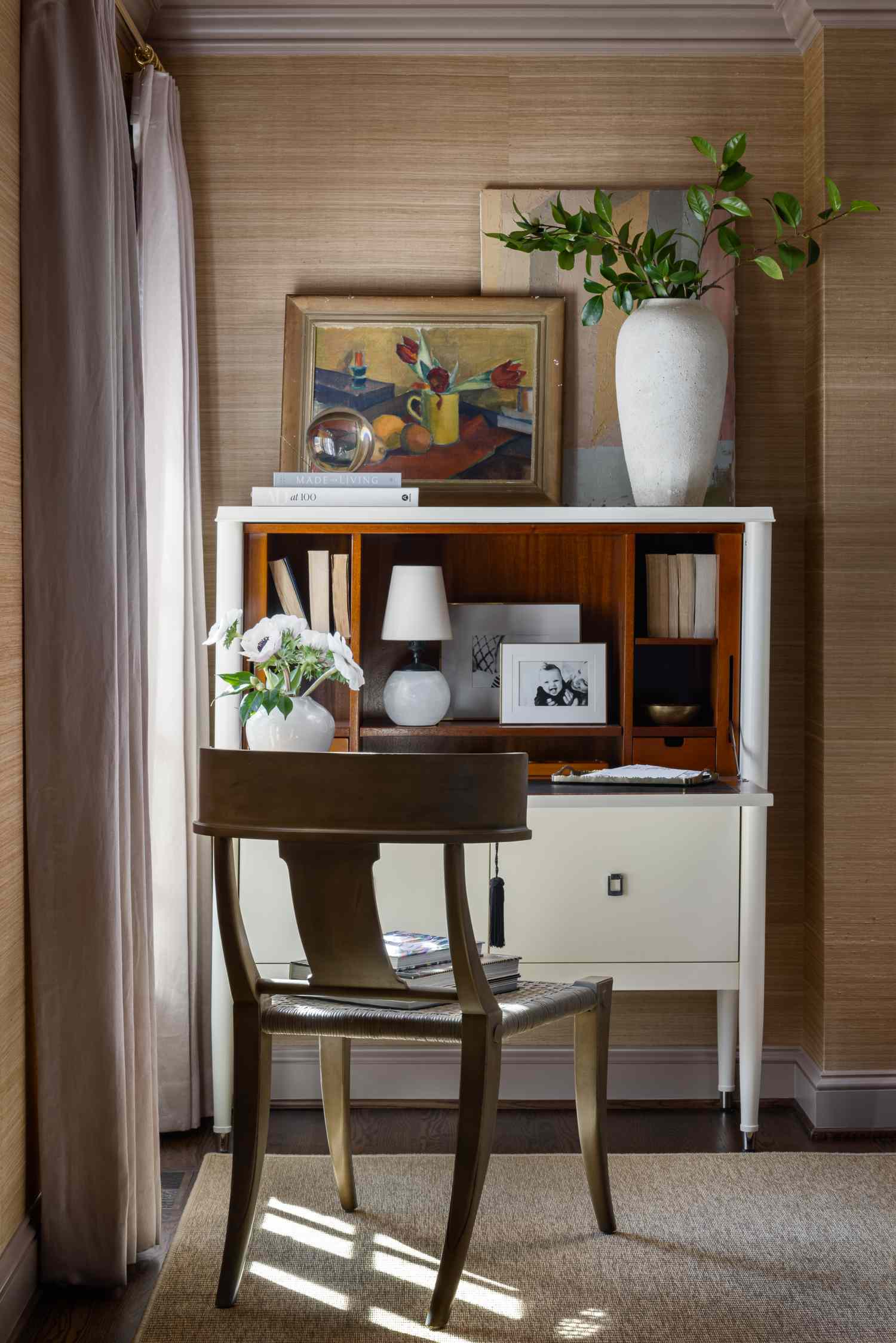 A home office setup with a desk chair lamp framed art and flower vases