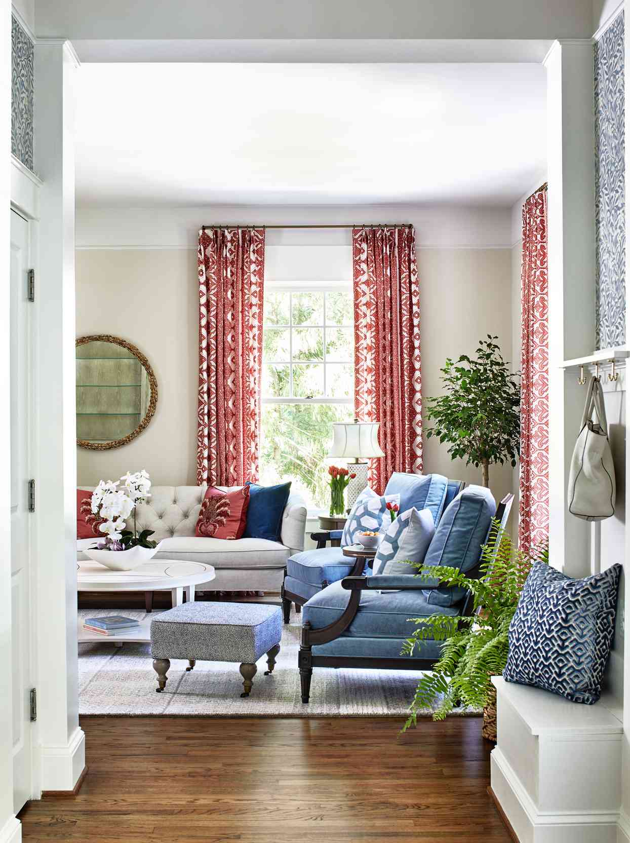 entryway overlooking neutral-colored living room with blue chairs and red accent pieces