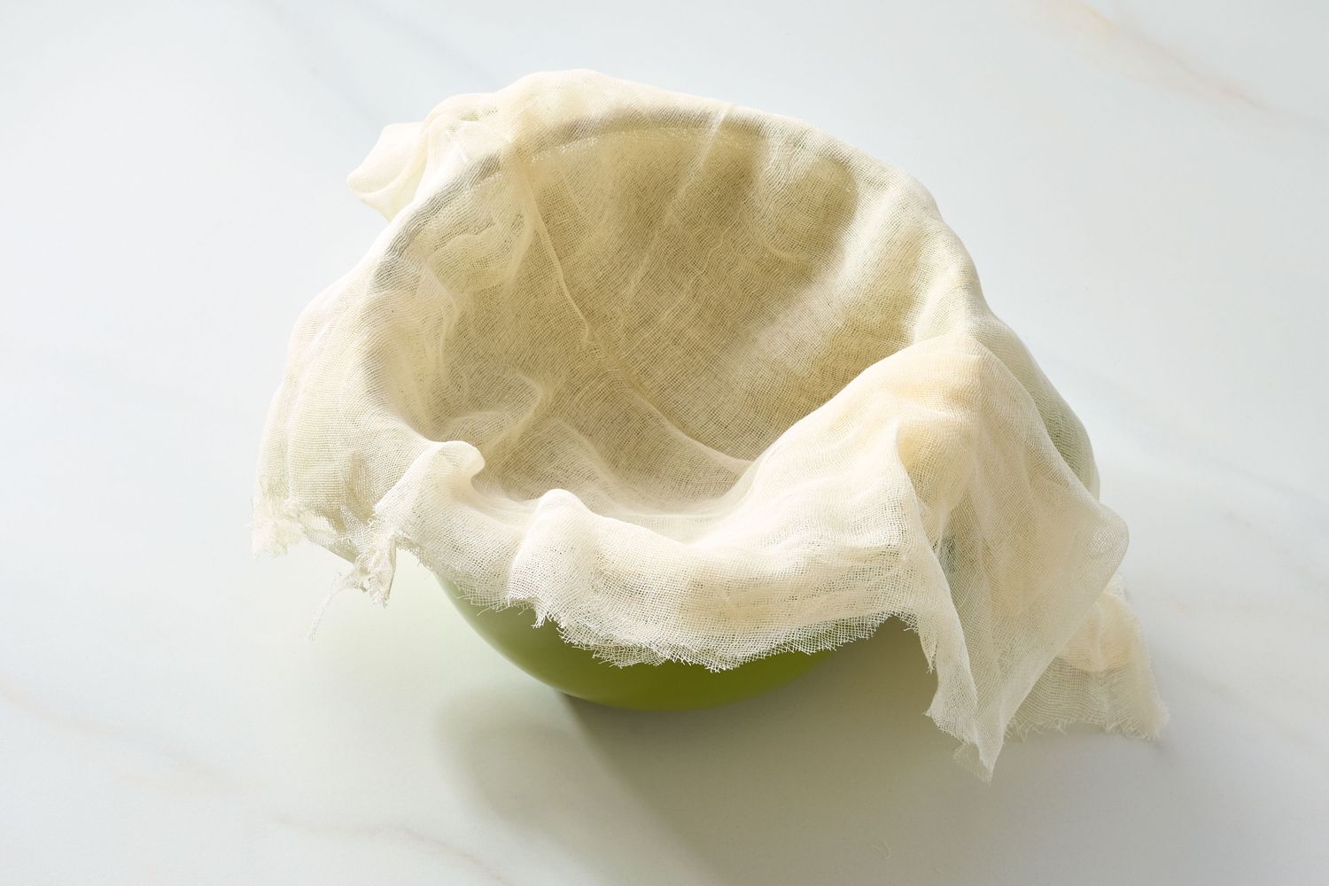 A green bowl lined with a piece of cheesecloth