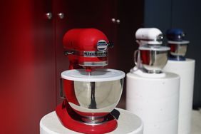 A red stand mixer displayed on a pedestal with other mixers in the background