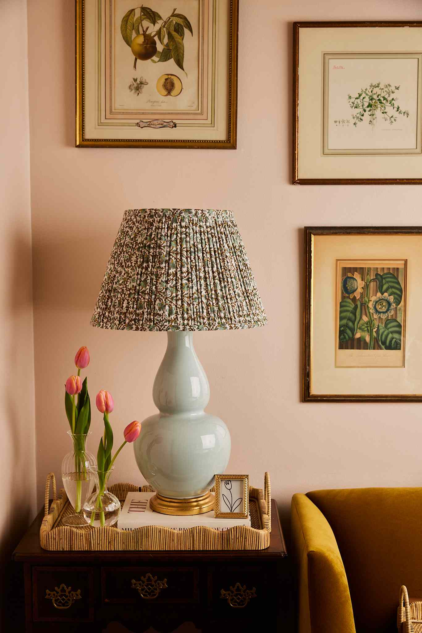 Table with a lamp pink tulips in a vase and framed botanical artwork on the wall