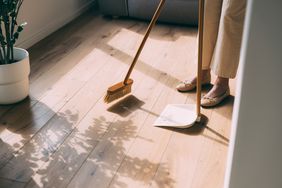 A person sweeping a wooden floor with a broom and dustpan
