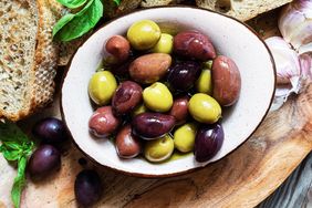 A bowl of assorted olives placed on a wooden surface near bread and herbs