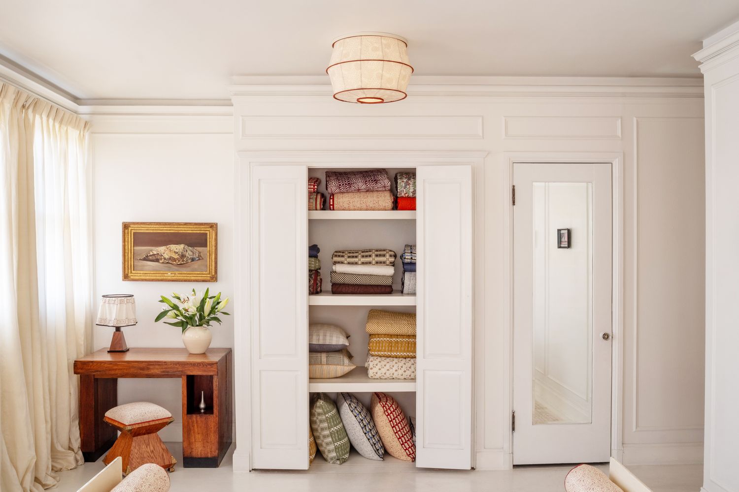 Interior with a builtin shelf containing folded linen a small desk setup and a door to the right