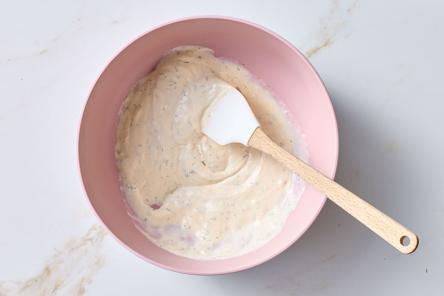 Mixing a creamy potato salad dressing in a bowl with a spatula