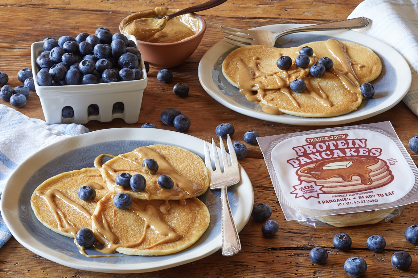 Plates of pancakes with peanut butter and blueberries Trader Joes Protein Pancakes packaging on the table