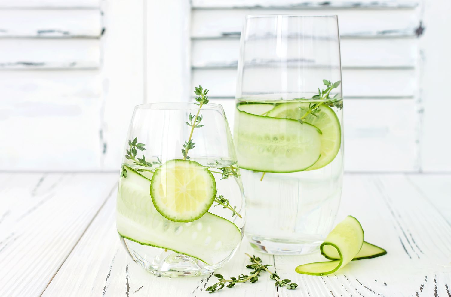 Glasses of infused water with cucumber slices and herbs on a light wooden surface