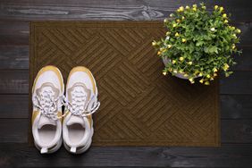 A pair of sneakers placed on a doormat next to a flowering plant