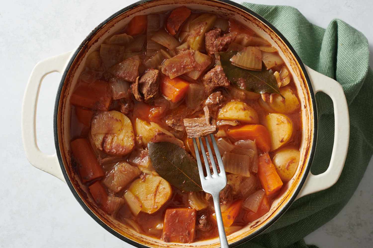 Beef stew in Dutch oven with piece of meat on a fork