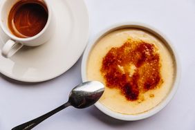 Crme brle with a spoon on a white surface beside a cup of espresso
