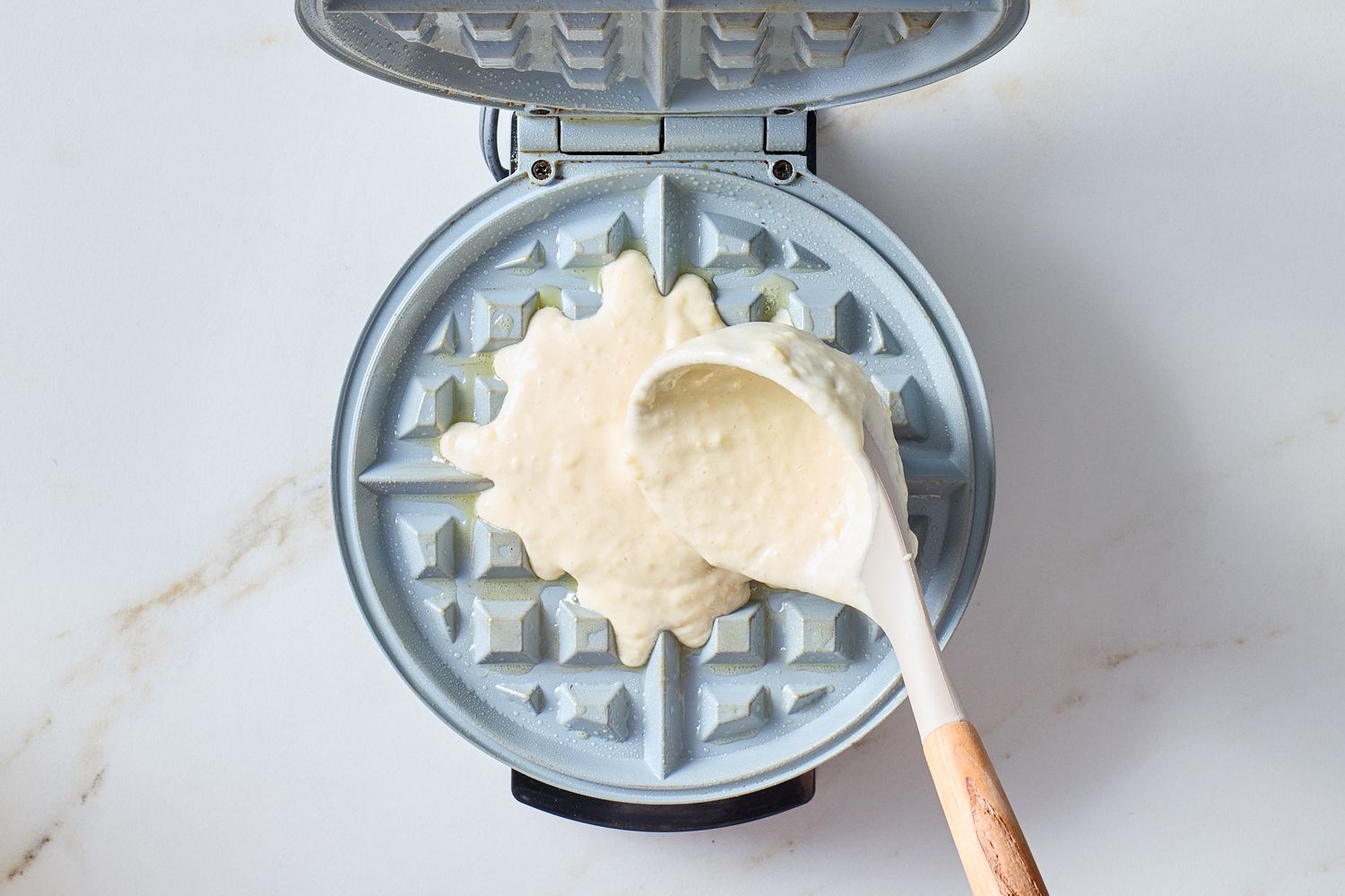 Batter being poured onto a waffle maker with a ladle