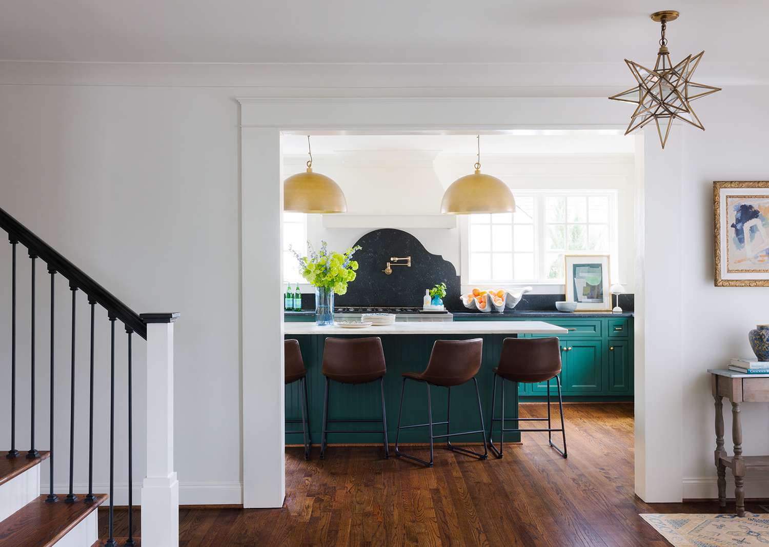 Kitchen design by Harper Harris Design | Photography by Laurey Glenn | Styling by Kathleen Varner: deep green cabinetry, arched black backsplash, brass accents, and airy white walls. A former breakfast nook was incorporated to maximize space and enhance functionality.