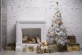 White Christmas tree with golden and silver balls, gift boxes, holiday decorations equipped fireplace, brick wall background