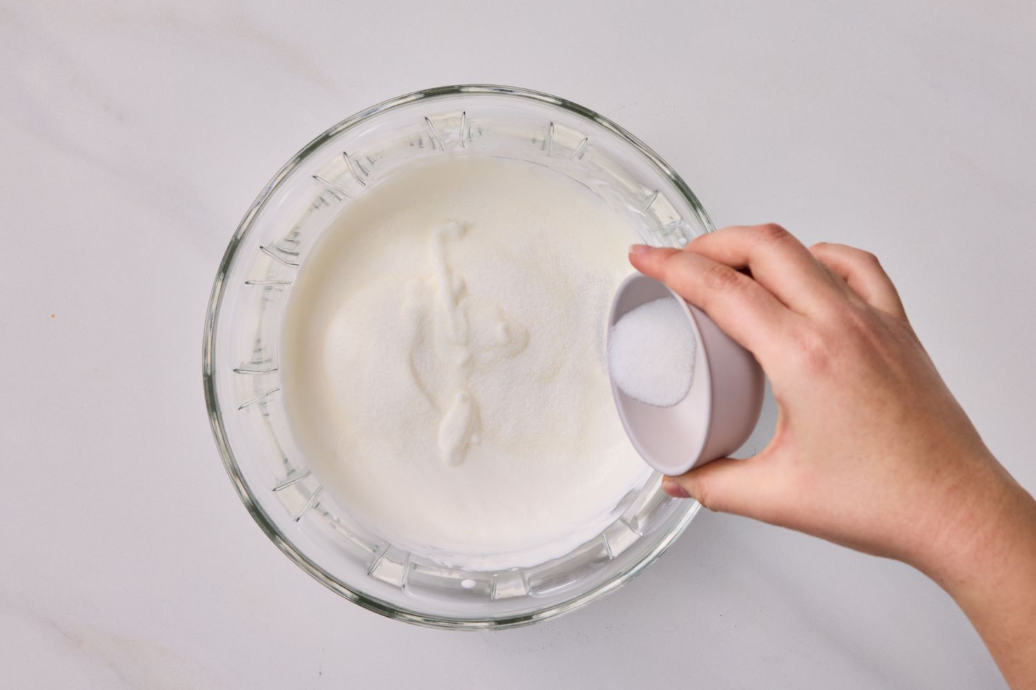 Hand pouring sugar into a bowl of whipped cream