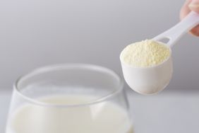 A measuring scoop of powdered supplement held above a glass of liquid