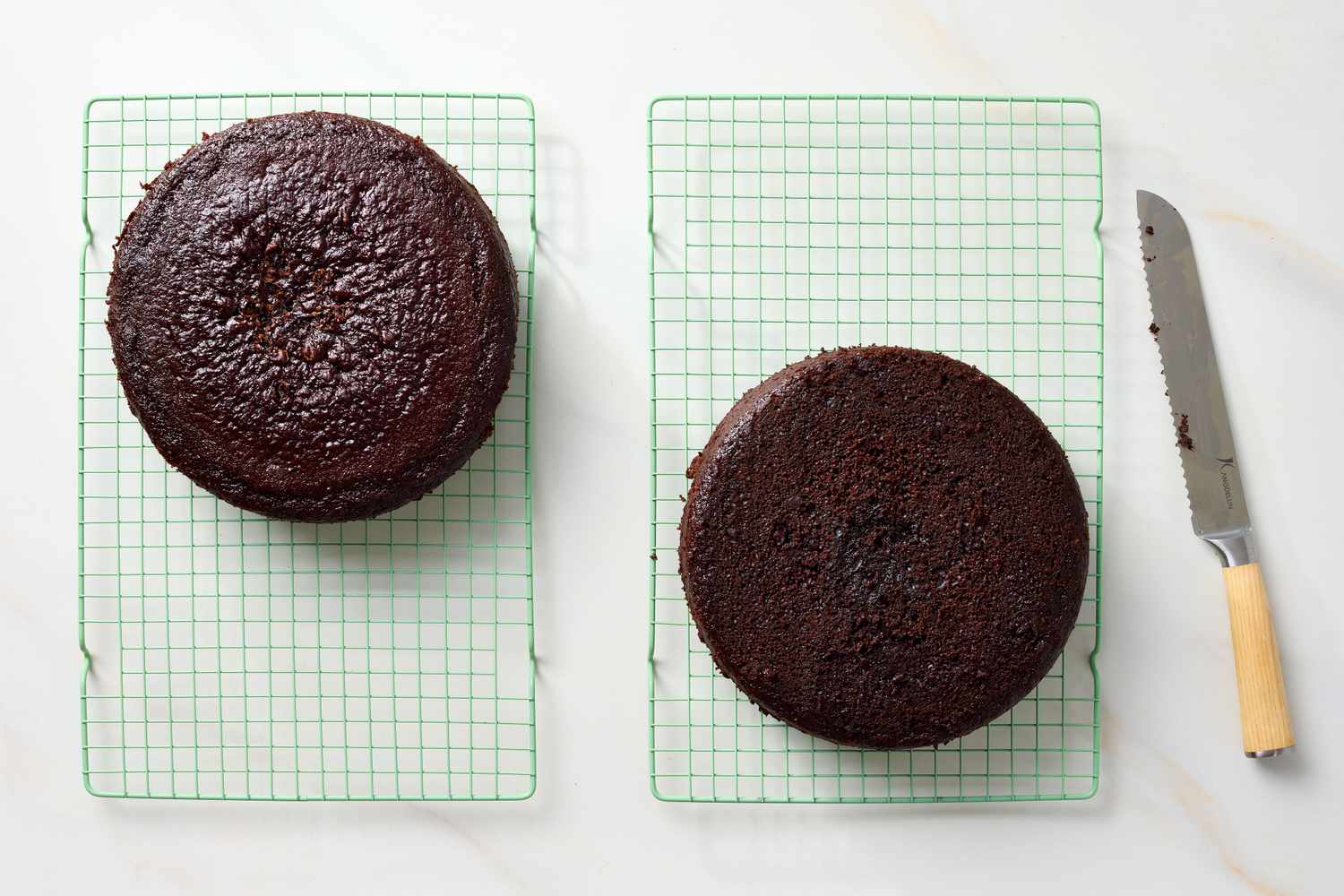 Two chocolate cake layers on cooling racks with a knife beside them