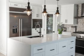 Black pendent lights over quartz counter top with over size stainless fridge in this newly renovated kitchen.