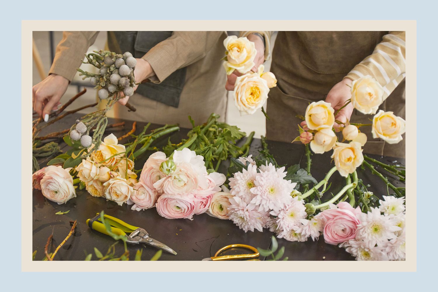 People arranging flowers on a table, with different flower types laid out