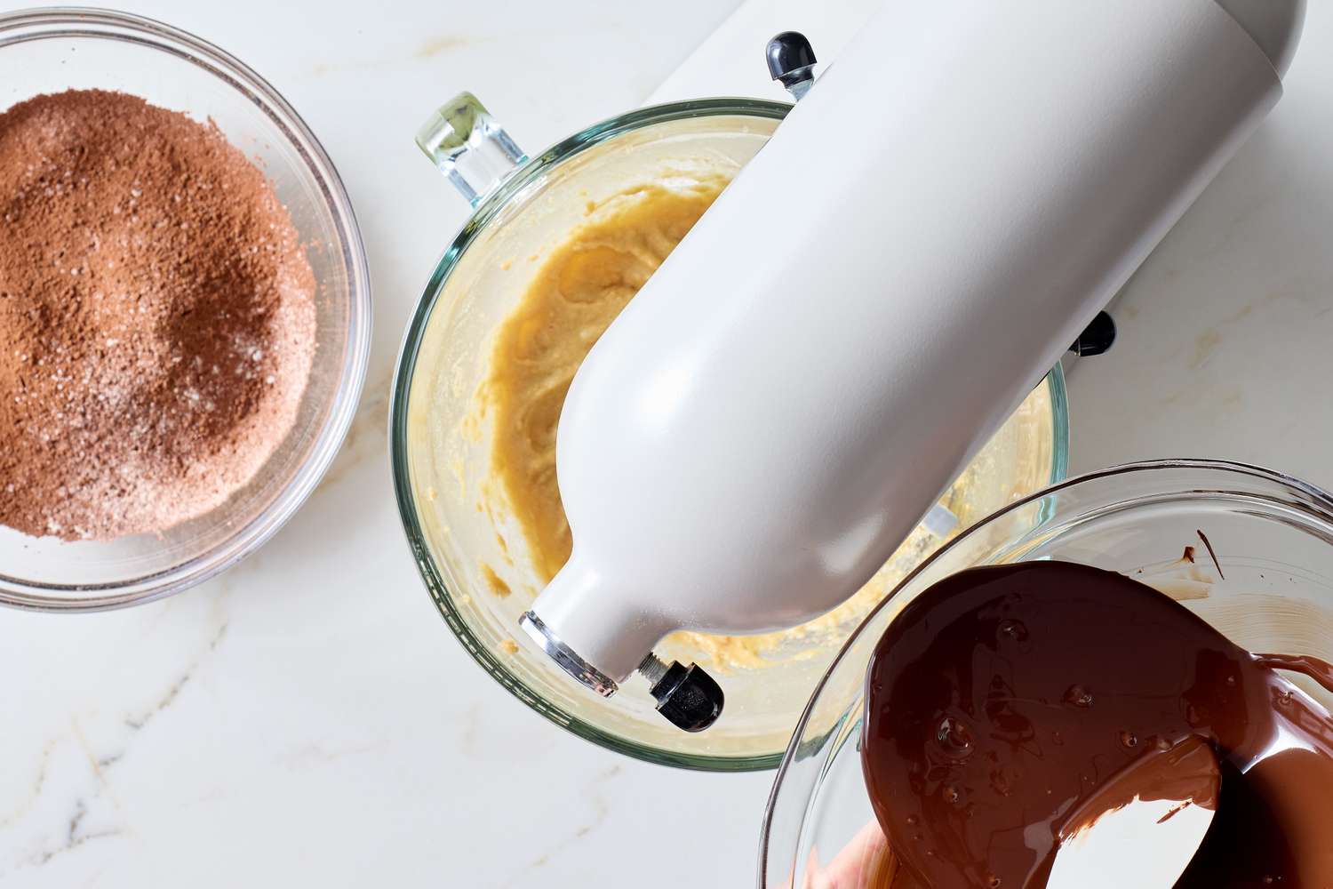 Mixing ingredients for chocolate cookies with a stand mixer and two bowls of batter and chocolate on the counter