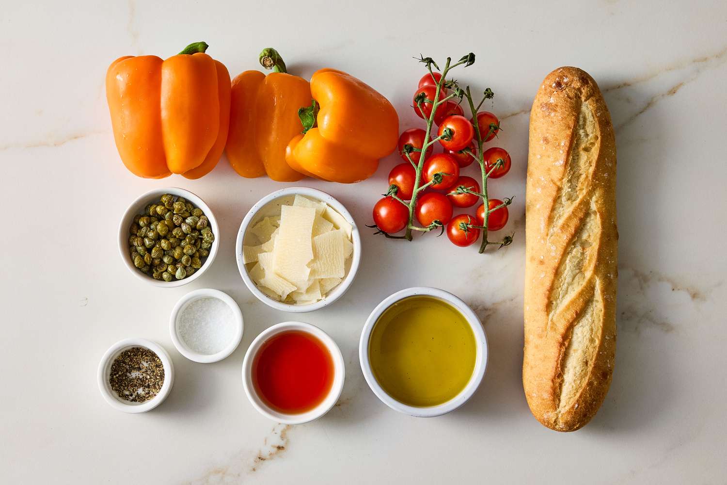 Ingredients for grilled pepper bruschetta include bell peppers cherry tomatoes baguette and small bowls with seasonings and oils