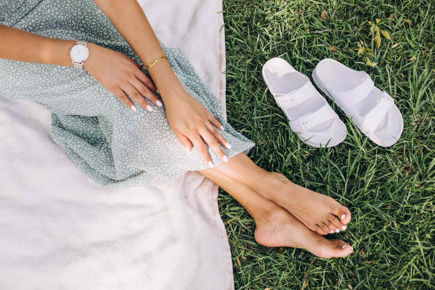 Hand and feet of a woman wearing a maxi dress on a picnic blanket in nature