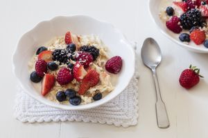 A bowl of oatmeal topped with berries and coconut with a spoon nearby on a textured mat