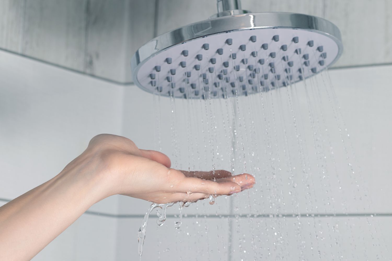 A hand checking water flow under a shower head